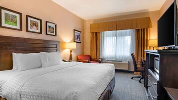 A hotel room with a large bed, a desk with a television, a chair, a desk lamp, and framed pictures on the wall.