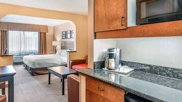 A hotel room with a bed, a desk, a chair, a microwave, a coffee maker, and a small kitchenette.