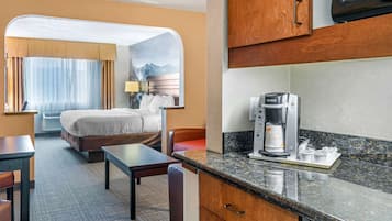 Habitación de hotel con cama, escritorio, silla, cafetera y vistas a montañas a través de la ventana.