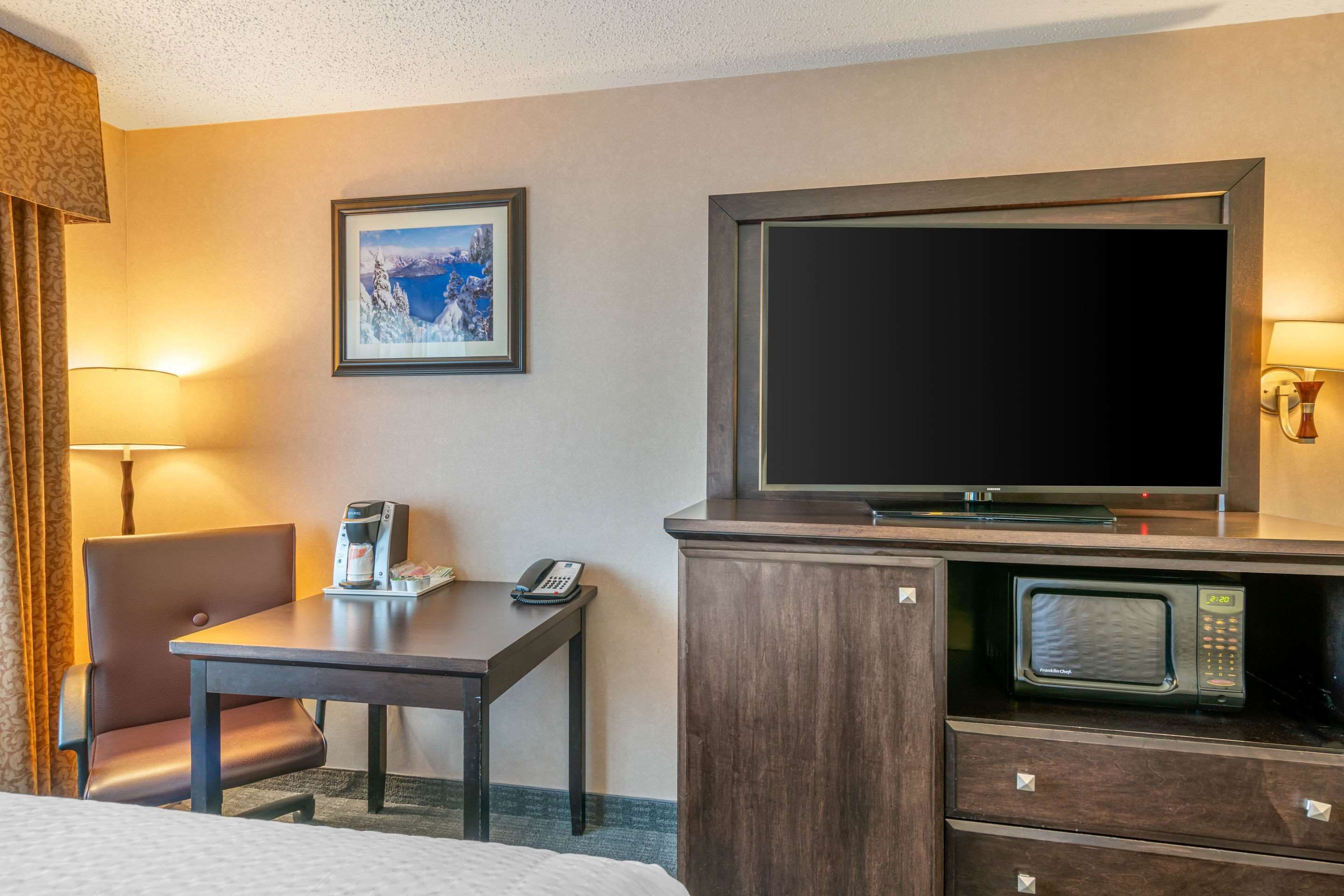 Ein Hotelzimmer mit einem Bett, einem Schreibtisch mit Telefon, einer Kaffeemaschine, einem Fernseher und einer Mikrowelle.