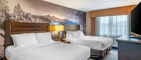 Ein Hotelzimmer mit zwei Betten, einem großen Wandgemälde mit einer Berglandschaft, einem Schreibtisch und einem Fernseher.