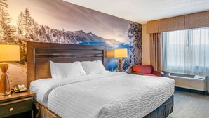 Una cama grande con cabecera de madera, dos lámparas de noche, un teléfono y una silla roja.