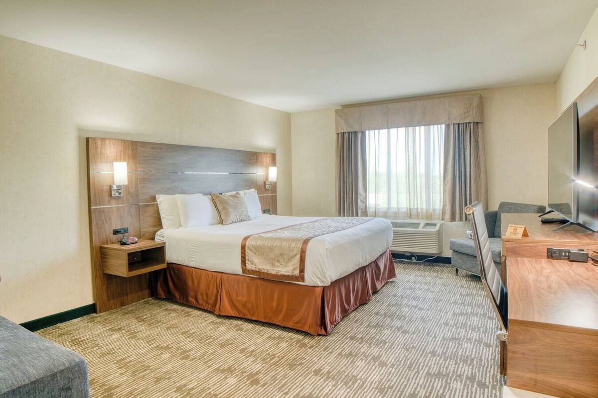 A hotel room with a large bed, a desk with a computer, a TV, and a window with curtains.