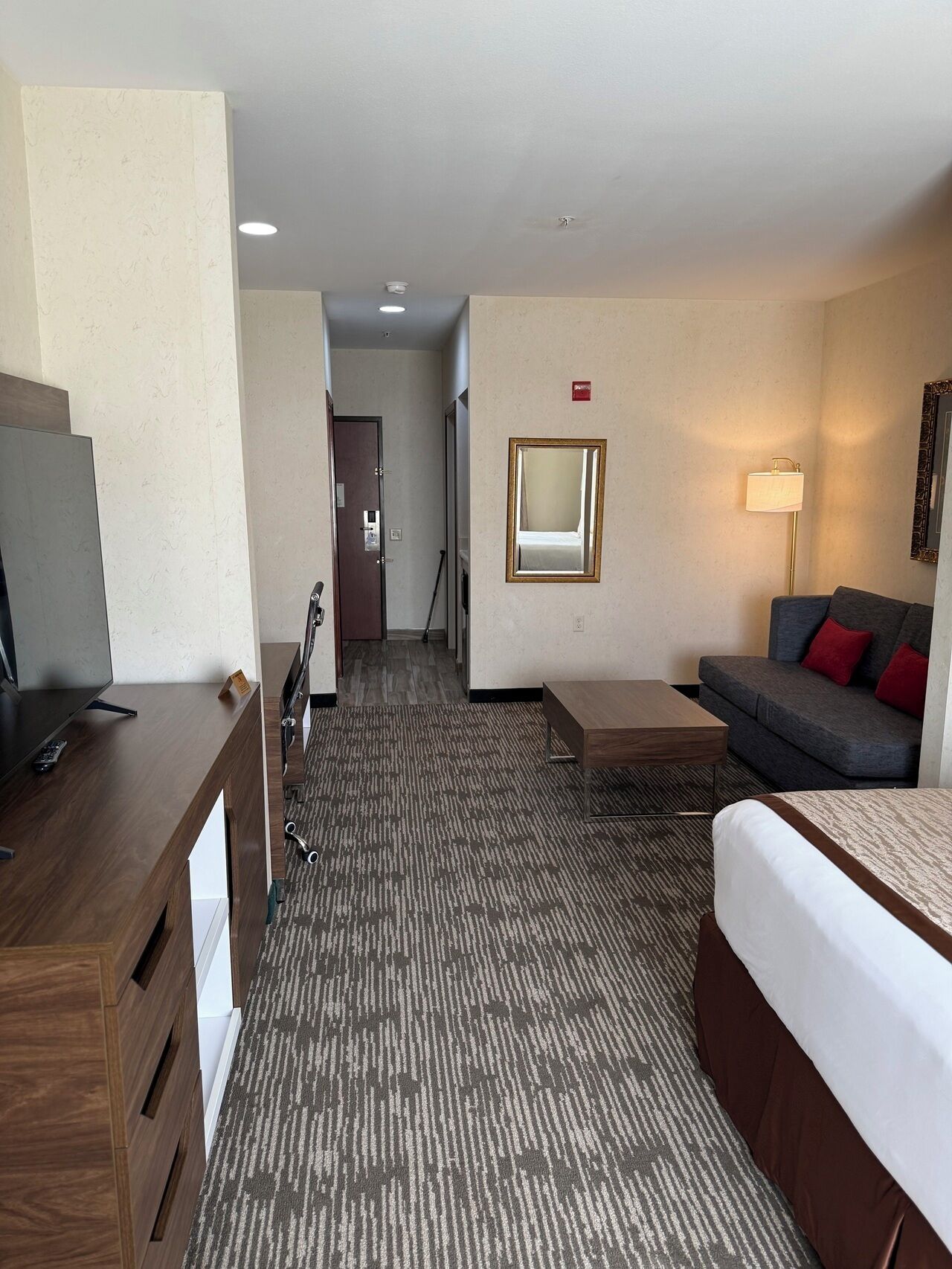 A hotel room with a bed, a sofa, a TV, a desk, and a carpeted floor.