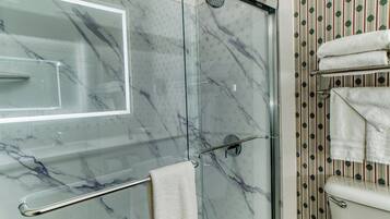 A glass-enclosed shower with a marble finish, a glass door, and a towel rack with folded towels.