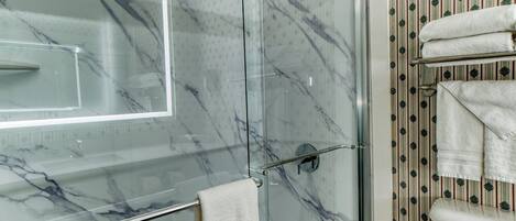 A glass-enclosed shower with a marble finish, a glass door, and a towel rack with folded towels.