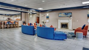 A spacious lobby with blue sofas, a fireplace, and a dining area with chairs and a table. - Evergreen Inn and Suites (Monroe)