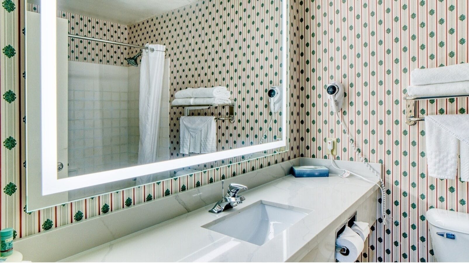 A bathroom with a large mirror, a sink, a toilet, and a shower.