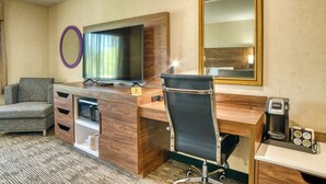 A hotel room with a wooden desk, a television, a chair, a microwave, a coffee machine, and a mirror. - Evergreen Inn and Suites (Monroe)