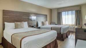 A hotel room with two beds, a desk, a lamp, and a window with curtains. - Evergreen Inn and Suites (Monroe)