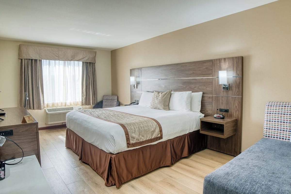 A hotel room with a large bed, a bedside table, a chair, a desk, and a window with curtains.