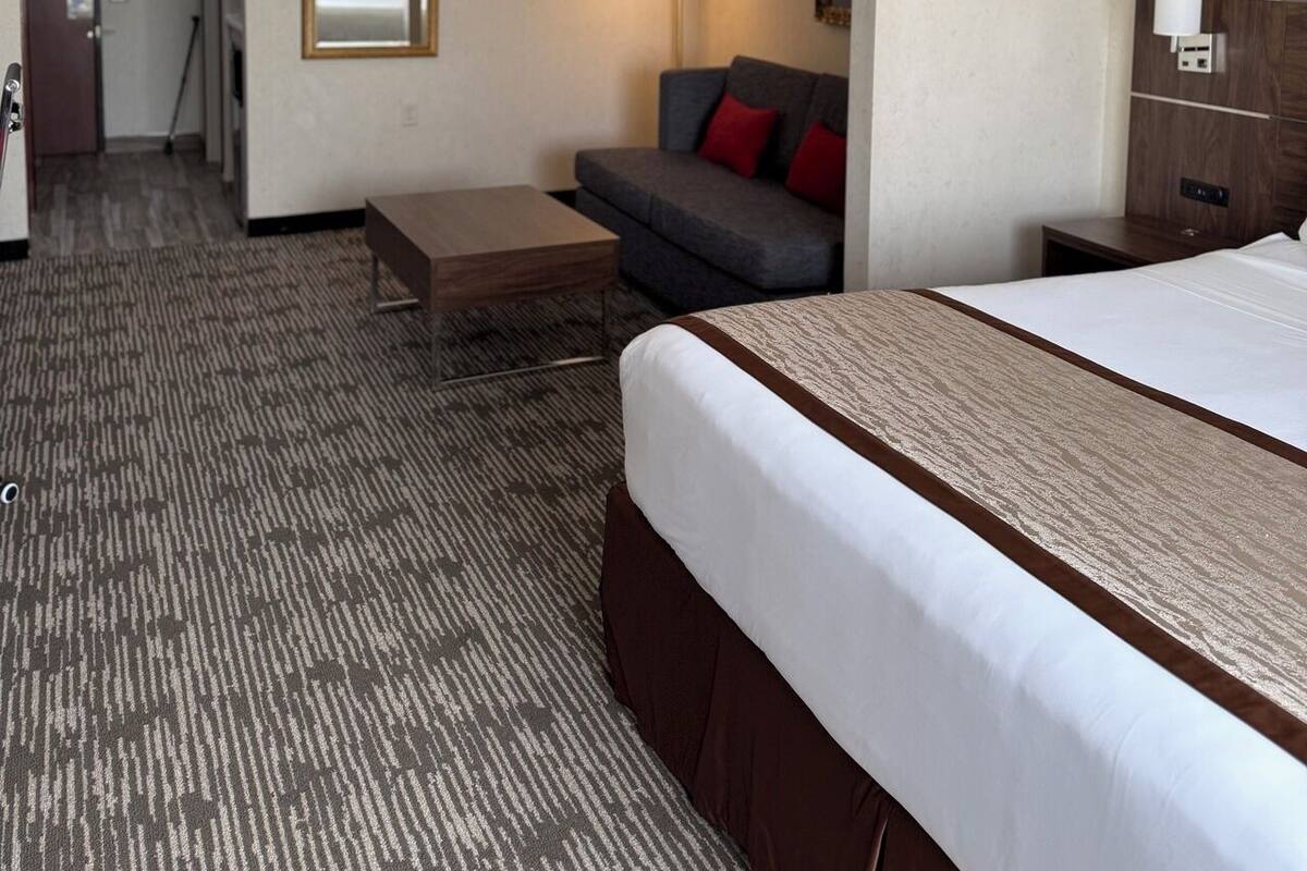 A hotel room with a bed, a sofa, a small table, and a lamp.