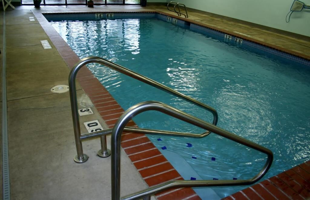 Una piscina interior con una escalera metálica y un borde con mosaicos.