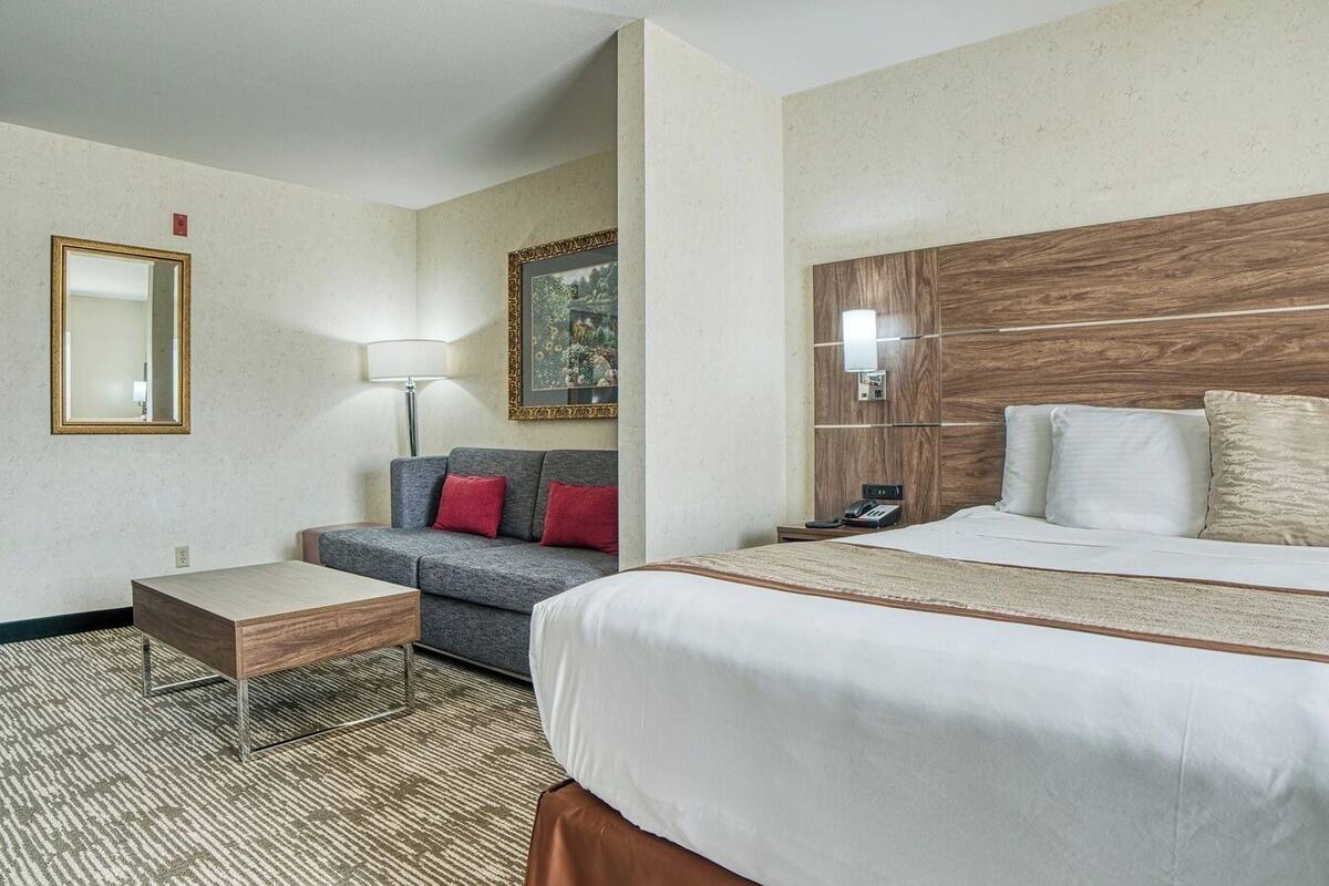 A hotel room with a large bed, a sofa, a small table, a lamp, and a painting on the wall.