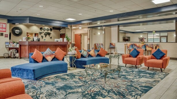 A spacious lobby with a reception desk, blue sofas, orange armchairs, and a patterned carpet. - Evergreen Inn and Suites (Monroe)