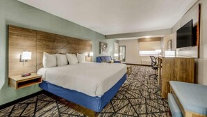 A hotel room with a large bed, a desk, a chair, a flat-screen TV, and a carpeted floor. - Clarion Pointe (Huntsville)