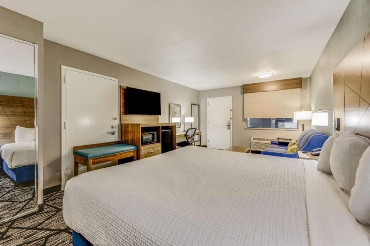 A hotel room with a large bed, a desk with a chair, a television, a mirror, and a door.