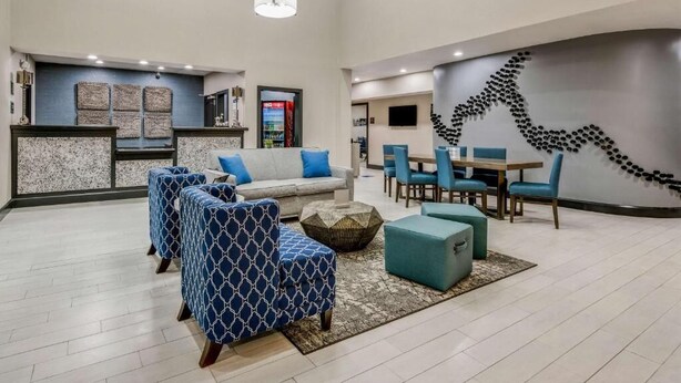 A spacious lobby with a reception desk, seating area with sofas and chairs, and a wall art installation. - Clarion Pointe (Huntsville)