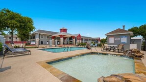 A pool area with lounge chairs, a building with a red roof, and a signboard. - Clarion Pointe (Huntsville)