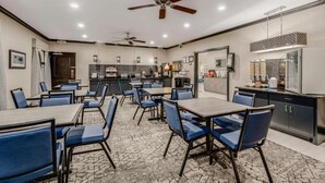 A dining area with tables and chairs, a kitchen in the background, and ceiling fans. - Clarion Pointe (Huntsville)