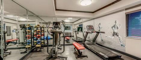 A gym with weightlifting equipment, treadmills, and a mirrored wall.