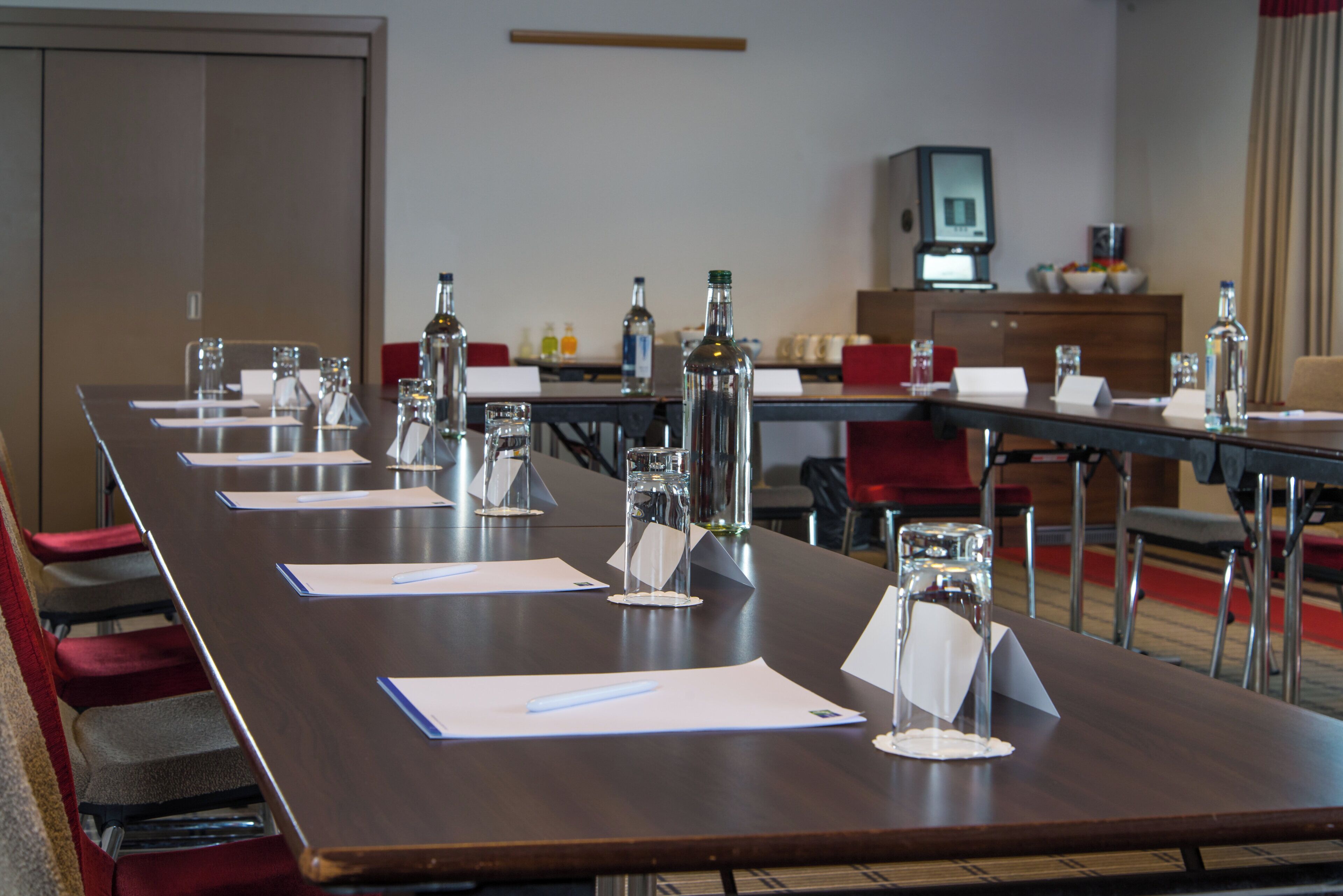 Une salle de conférence avec une longue table, des chaises, des plaques nominatives et des bouteilles d’eau.