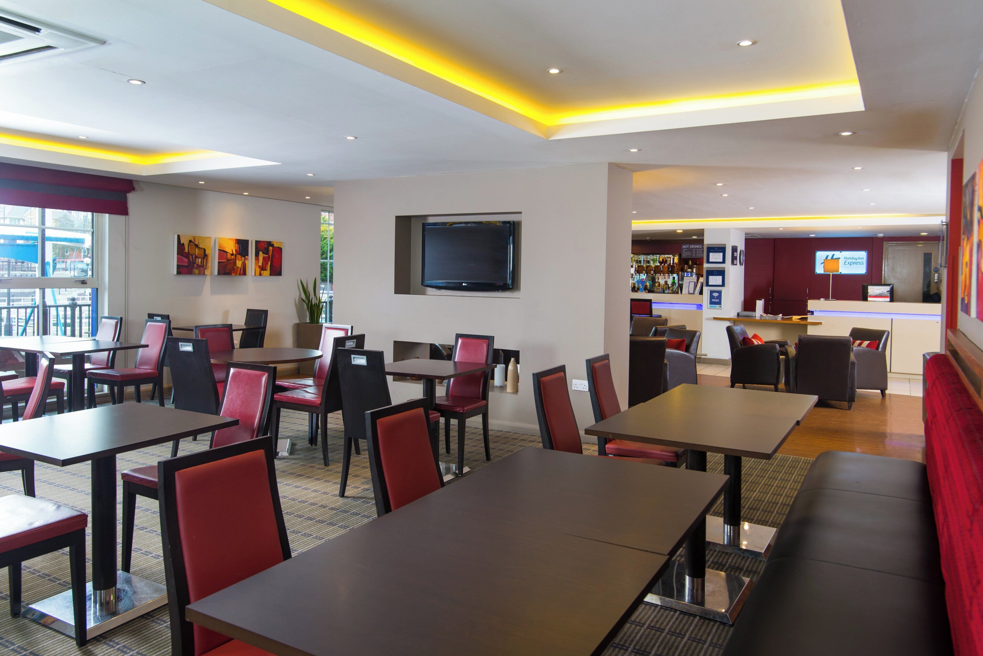 Un'area ristorazione dell'hotel con tavoli, sedie, un bar e una televisione appesa al muro.