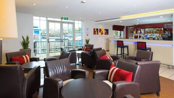 A hotel lobby with leather seating, a bar area, and large windows offering a view of the outside.