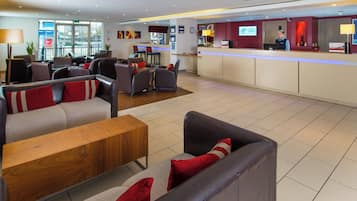 A hotel lobby with seating areas, a reception desk, and a view of the outside.