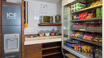 A kitchenette with an ice dispenser, microwave, and a refrigerator stocked with snacks and beverages.