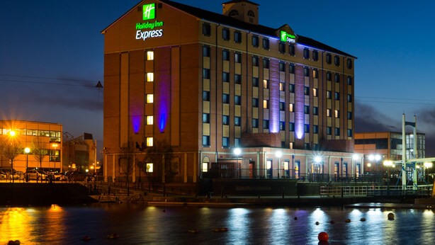 Et Holiday Inn Express hotel med en stor bygning, mange vinduer og udsigt til vandet.