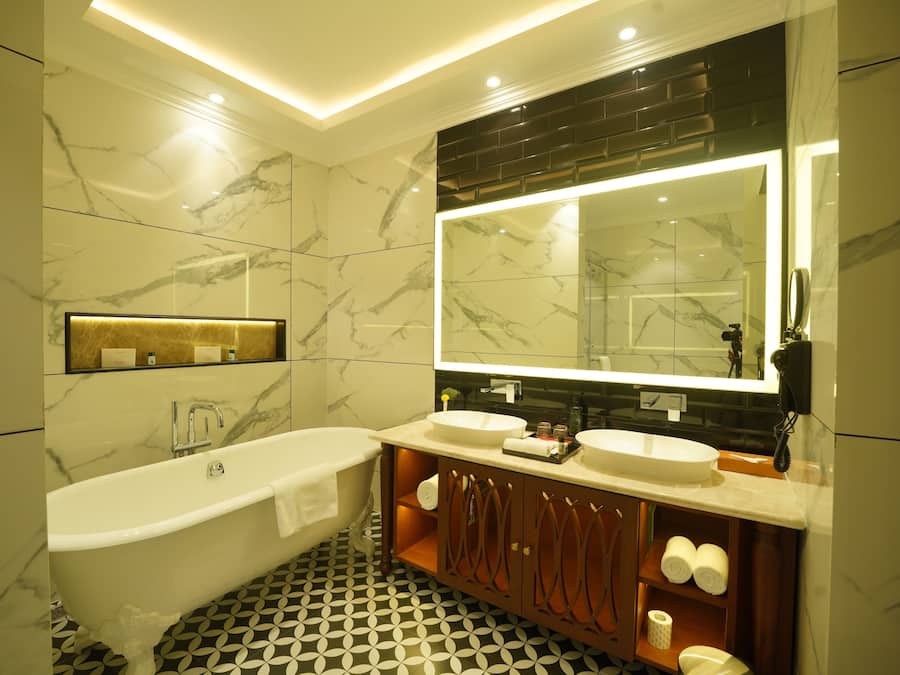 A modern bathroom with a freestanding bathtub, two sinks, a large mirror, and marble-patterned walls.