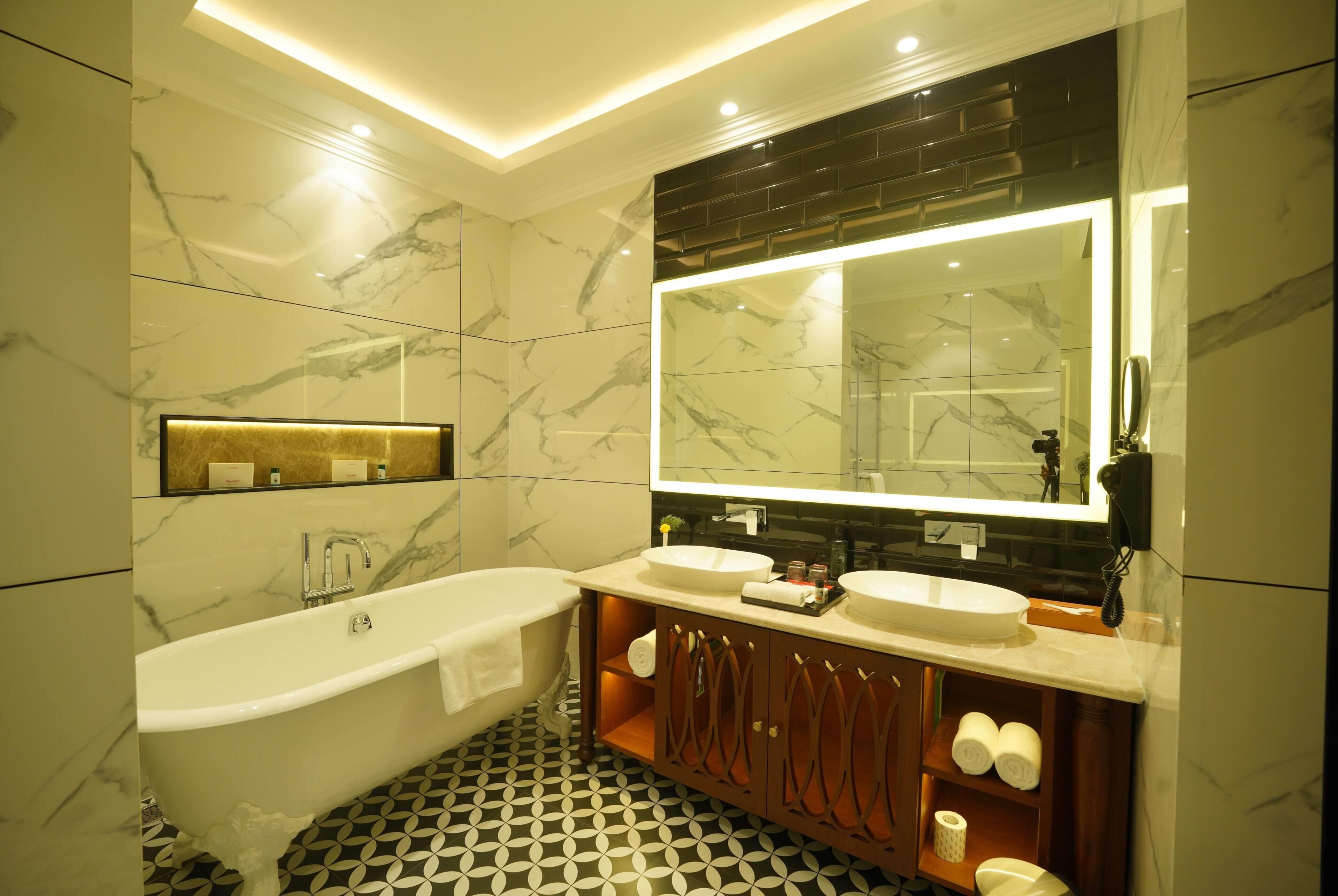 Un baño moderno con una bañera independiente, dos lavabos, un espejo grande y paredes de mármol.