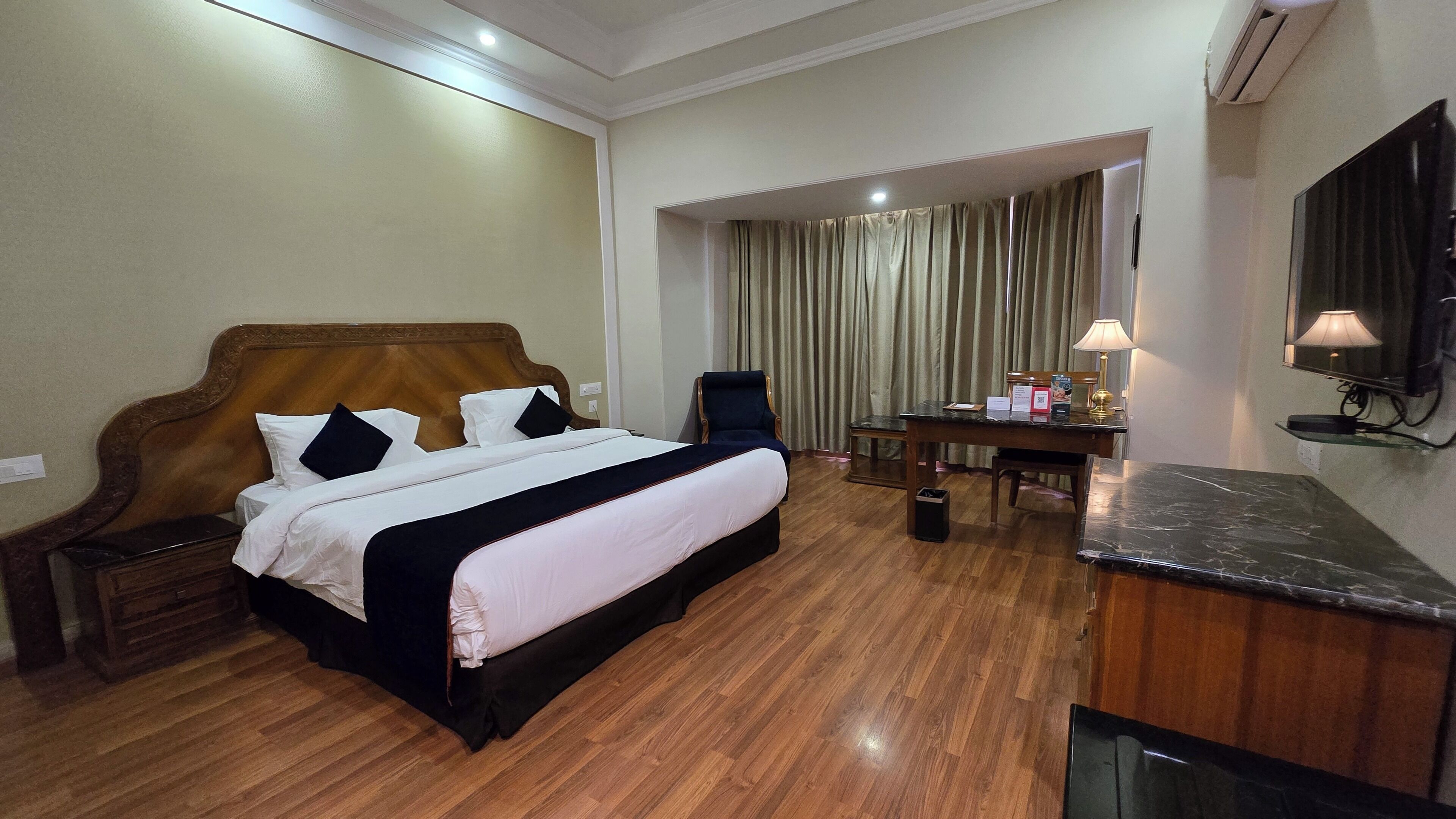 A hotel room with a large bed, a desk with a lamp, a chair, and a television.