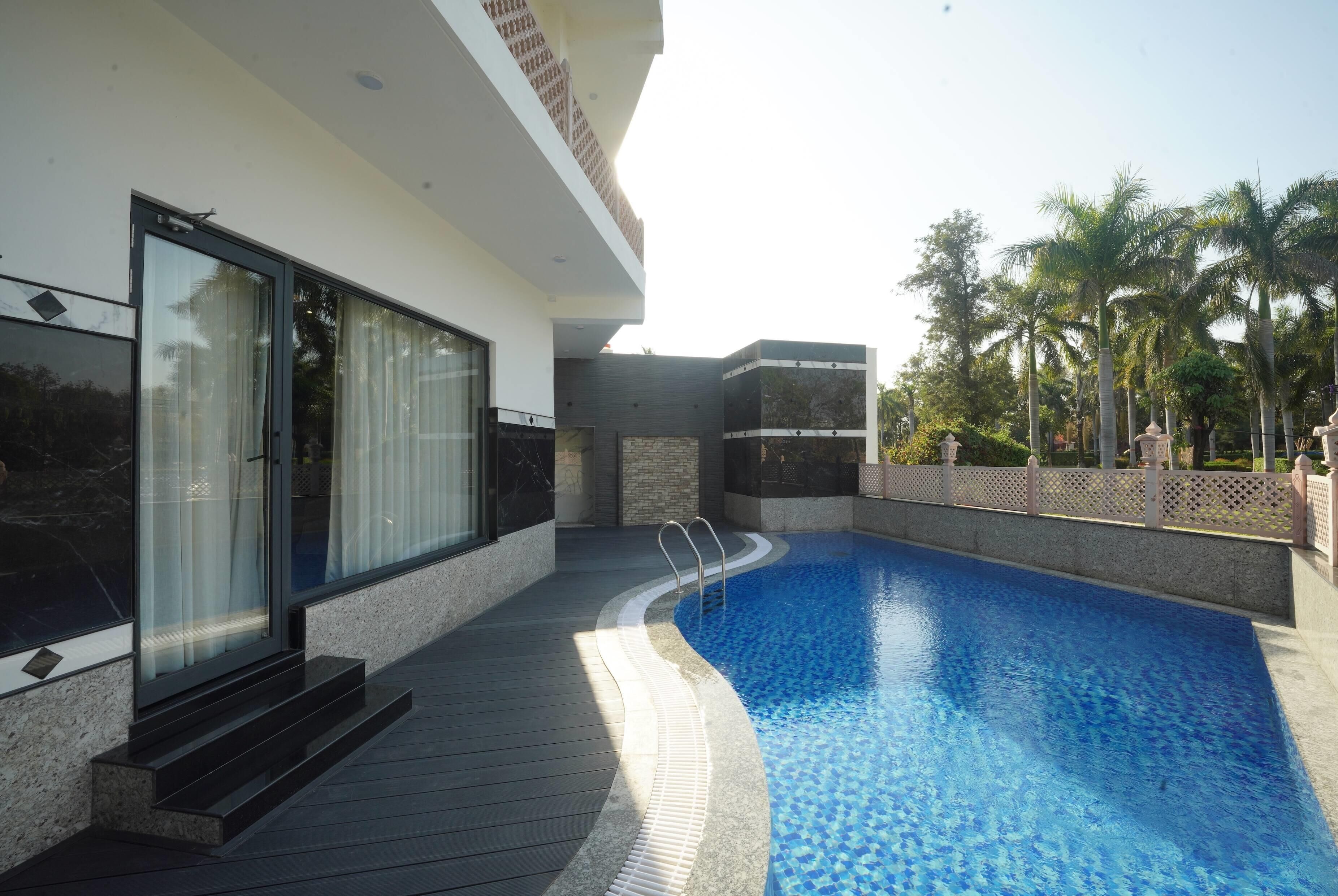 Un espace piscine moderne avec une piscine à l’eau d’un bleu limpide, une terrasse en bois et une porte vitrée donnant sur un patio abrité.
