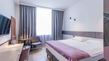 A hotel room with a bed, a desk, a chair, a TV, and a window with curtains.