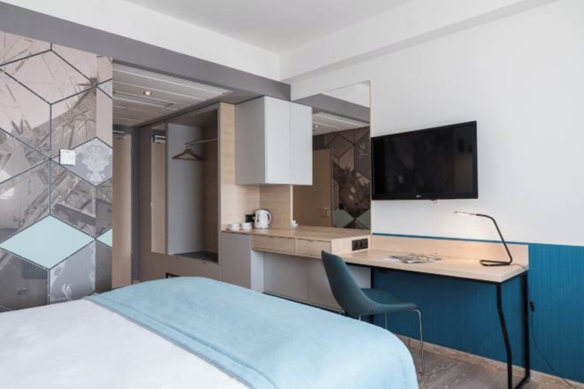 Una habitación de hotel moderna con cama, escritorio, silla, televisión y armario.