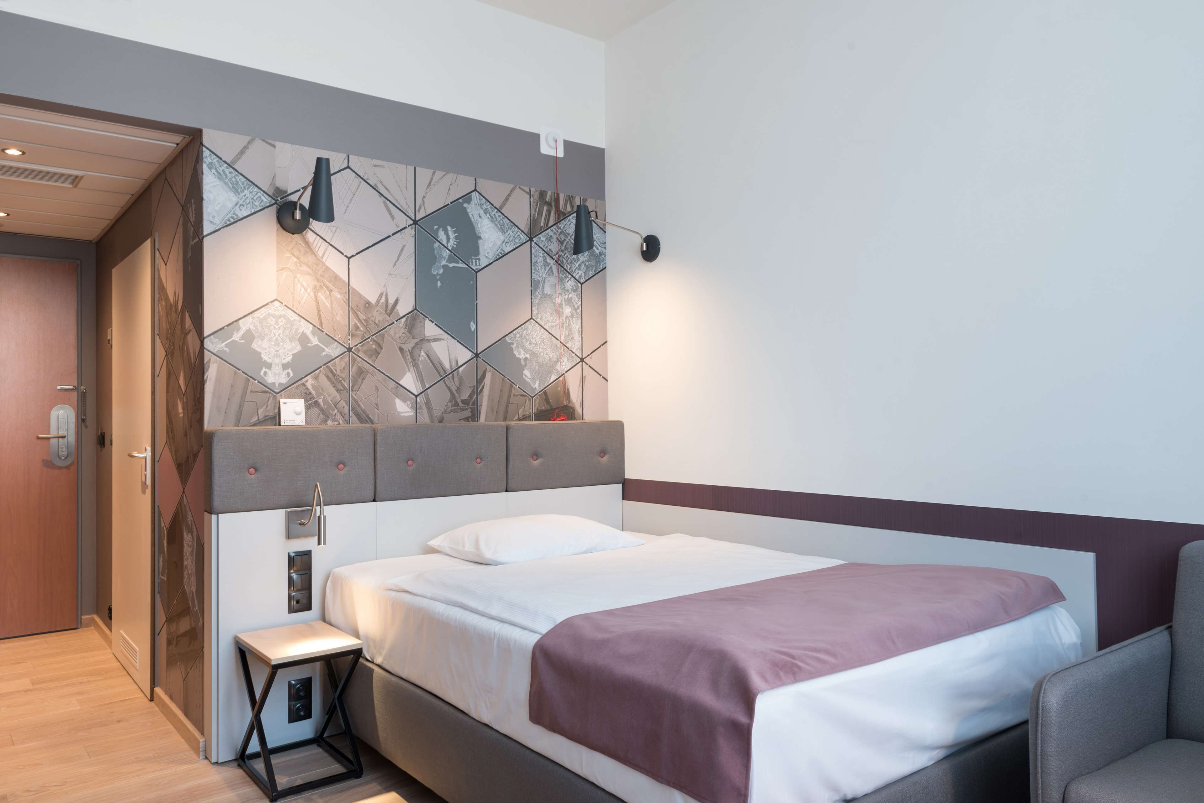 A modern hotel room with a bed, a small table, and a wall with geometric patterns.