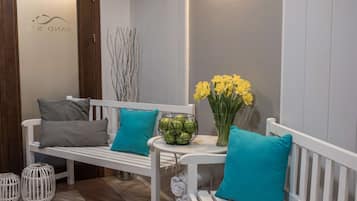 Um banco branco com almofadas cor-teal, uma cesta branca e um vaso com flores amarelas num saguão de hotel.