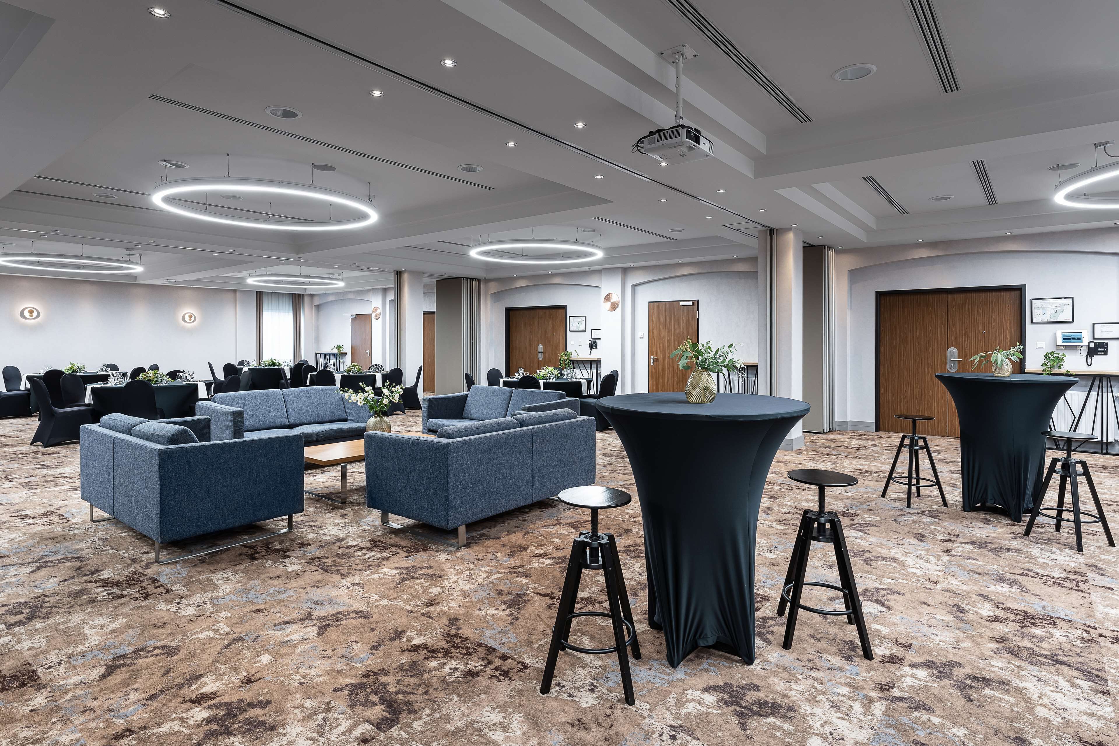 A spacious conference room with modern furniture, including sofas and round tables, and a carpeted floor.