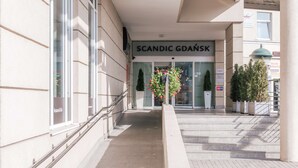 La entrada al Scandic Gdańsk, con fachada moderna, ventanas grandes y una escalera que conduce a la entrada.