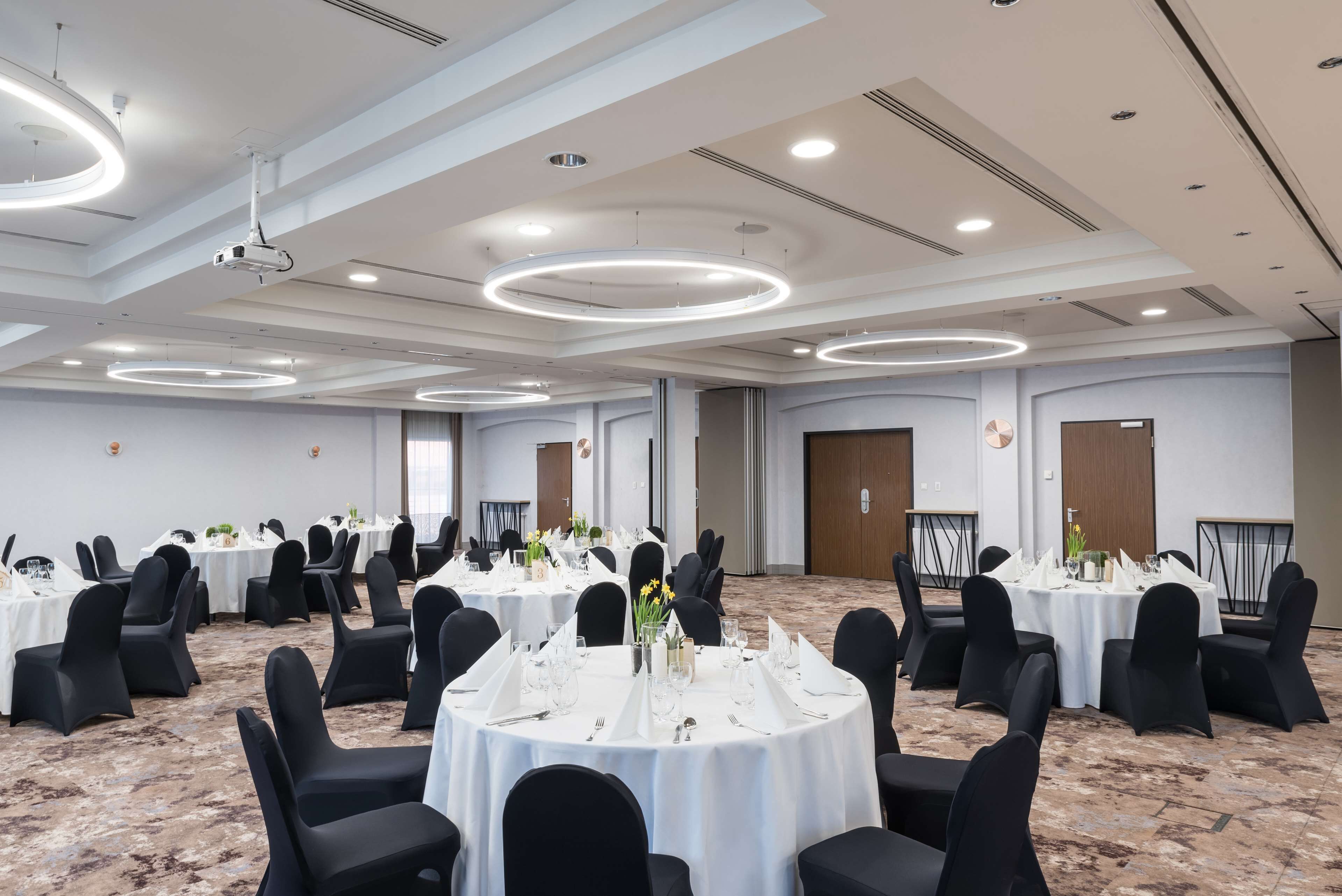 A large conference room with multiple round tables, black chairs, and white tablecloths.