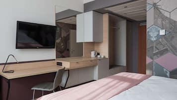 Una habitación de hotel moderna con una cama, un escritorio con una silla, un televisor y un armario.