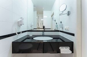 A modern bathroom with a black and white tiled design, a round sink, a mirror, and a hairdryer on the wall.