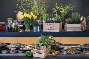 A buffet table with various food items, a wooden box labeled 'ROCCATO', and decorative plants. - Scandic Gdansk (Gdansk)