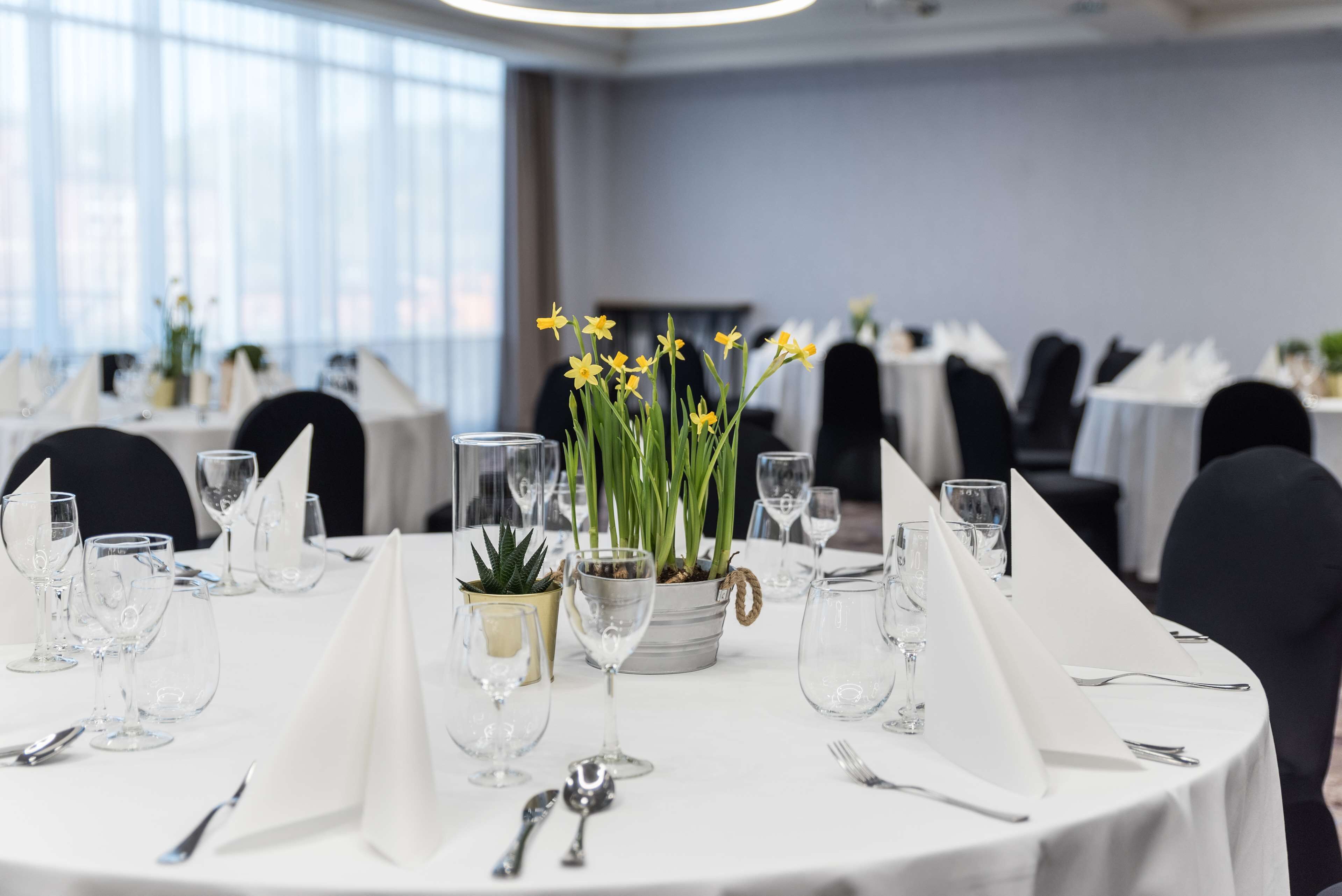 Una mesa de comedor preparada para un evento formal, con manteles blancos, cristalería transparente y un centro de mesa con flores amarillas.