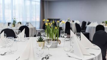 Una mesa de comedor preparada para un evento formal, con manteles blancos, cristalería transparente y un centro de mesa con flores amarillas.