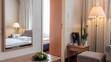 Quarto de hotel com uma cama, uma escrivaninha com abajur, uma cadeira, uma mesinha com maçãs e um espelho refletindo o quarto.