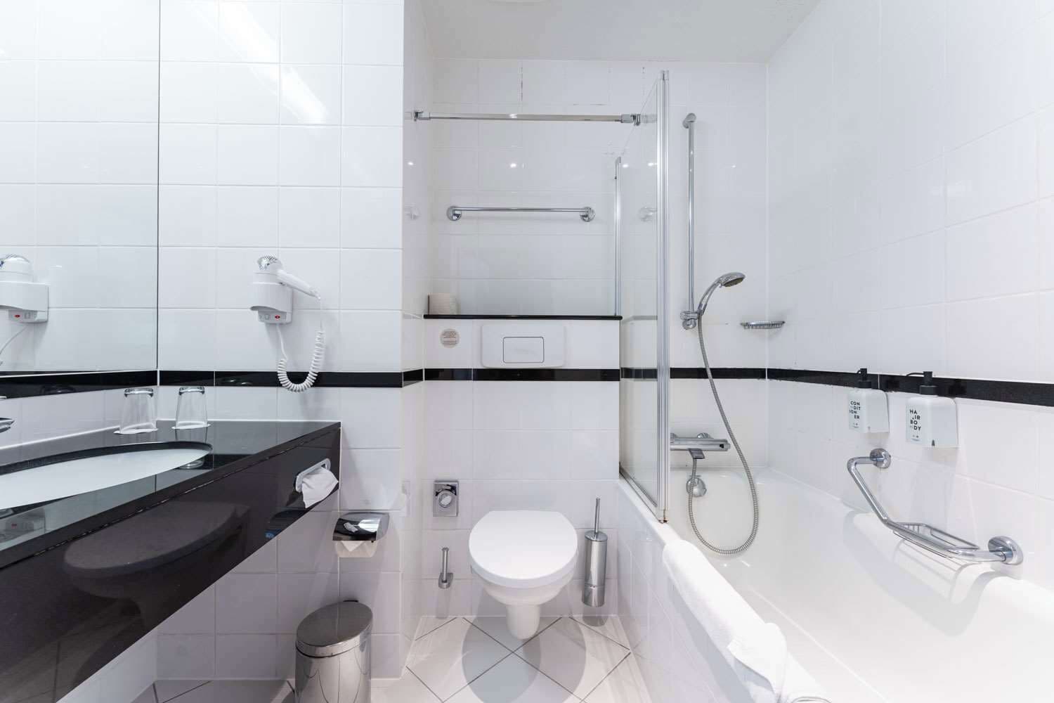 Une salle de bain moderne avec une douche à parois de verre, un lavabo sur un plan de toilette noir, des toilettes et une baignoire.