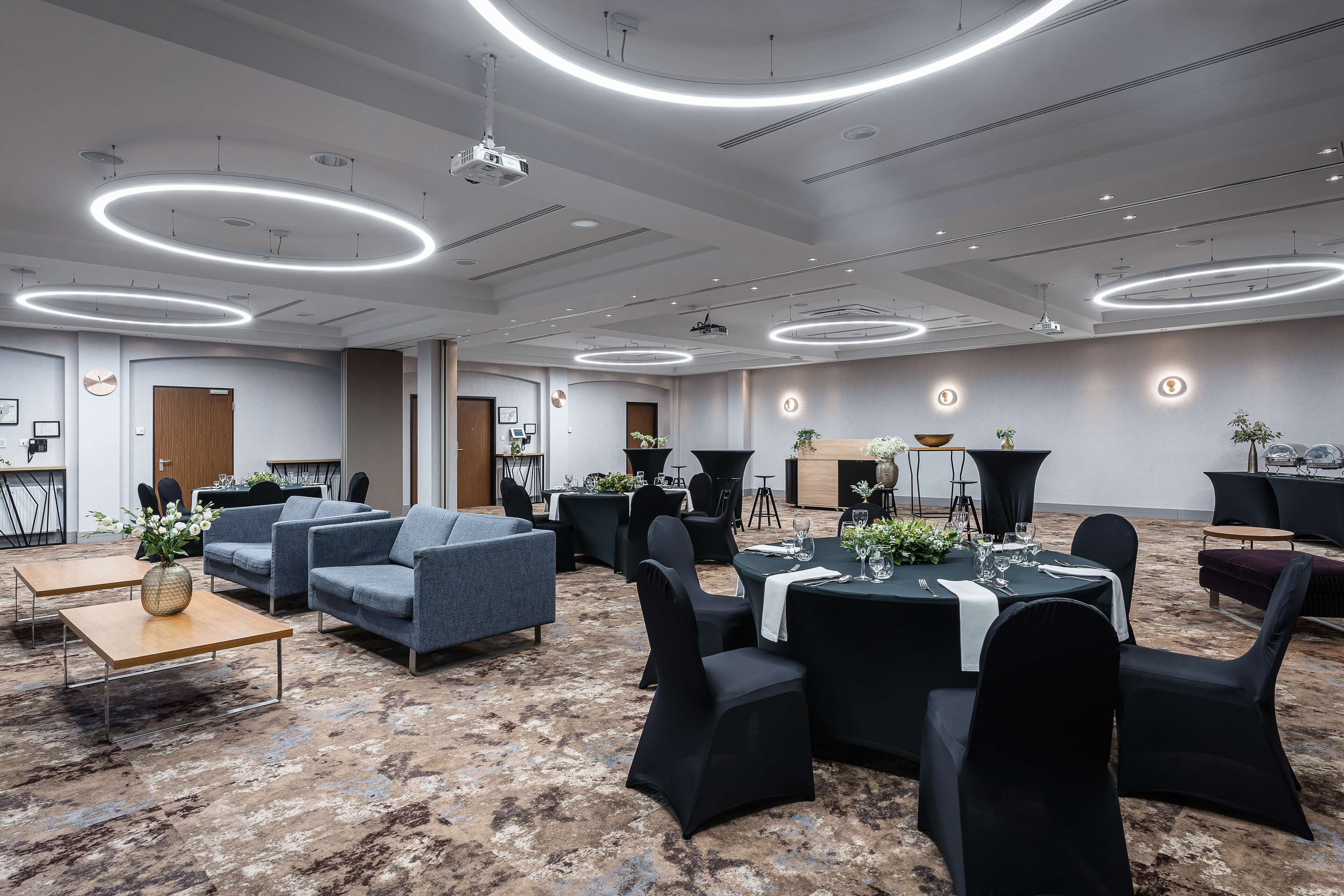 Une salle de conférence moderne, dotée de tables rondes, de chaises noires et d’un sol recouvert de moquette.